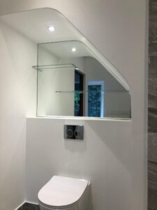 Custom cut bathroom mirror with integrated glass shelf and angled edge detail
