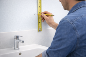 Marking wall measurements with a tape measure and pencil for a custom bathroom mirror